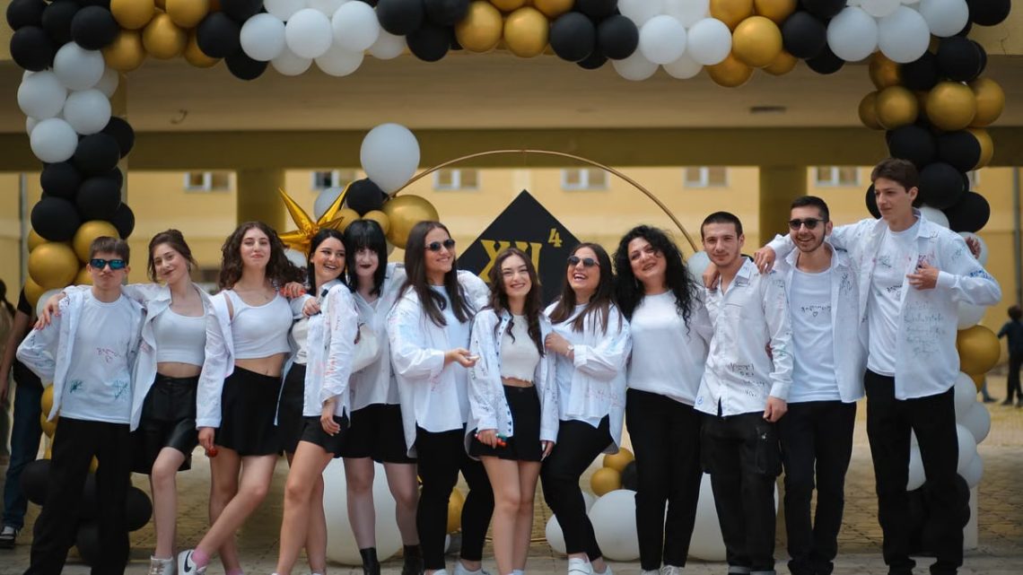 A group of teenagers posing under a balloon arch outdoors at a school celebration.
