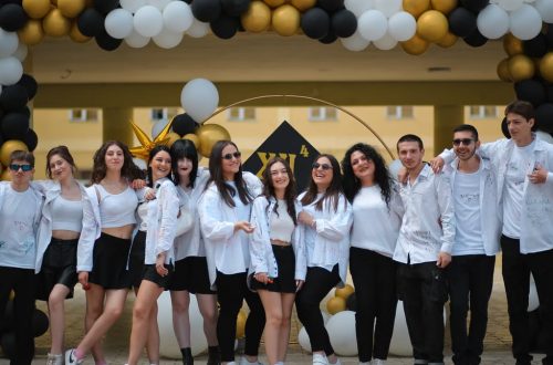 A group of teenagers posing under a balloon arch outdoors at a school celebration.
