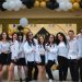 A group of teenagers posing under a balloon arch outdoors at a school celebration.